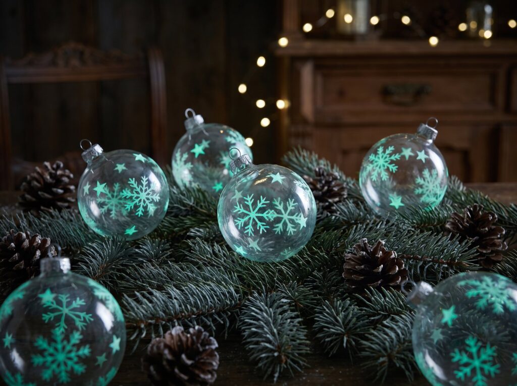 Gläserne Christbaumkugeln mit leuchtend gemalten Schneeflocken auf Tannenzweigen